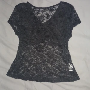 Svart spetsblus från SHEIN Teen - Svart transparent blus från SHEIN Teen i storlek 14Y / 158-164. Hela toppen är i tunn spets med blommigt mönster och v-ringning. Korta ärmar och figurnära passform, perfekt för att skapa en cool och trendig look.