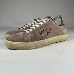 Saint Laurent mocka sneakers brun - Snygga sneakers från Saint Laurent i brun mocka med handskriven logga på sidan. Skorna har vita snören, rund tå och en klassisk platt sula i gummi. Perfekta för dig som gillar en stilren men ändå edgy look.