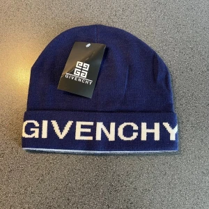  Givenchy mössa - Snygg marinblå mössa från Givenchy med vit logotyp runt kanten. Tillverkad i mjukt stickat material som håller dig varm och ger en clean look. Perfekt accessoar för att lyfta din outfit med en exklusiv touch.