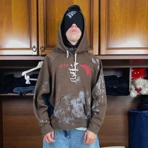 Swag hoodie  - Säljer en brun hoodie från All Star med svart och röd grafik, vita snören och unika patchar på ryggen. Hoodien har känguruficka, kontrastpaneler och coolt sliten look med vita detaljer. Perfekt för dig som gillar streetwear och statement-plagg.