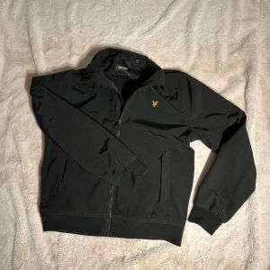 Svart bomberjacka från Lyle & Scott - Svart bomberjacka från Lyle & Scott med klassisk gul fågel-logga på bröstet. Jackan har dragkedja framtill, ribbade muddar och två sidofickor. I storlek M              ✅ skriv för frågor mått eller mer bilder✅