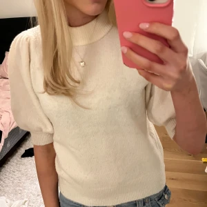Vit stickad tröja från ONLY - Supersöt vit stickad tröja från ONLY med puffärmar och hög ribbad hals. Mjuk och skön, perfekt till jeans eller kjol. Tröjan har en clean look och är lätt att matcha med olika stilar. Passar dig som gillar enkel men trendig design.