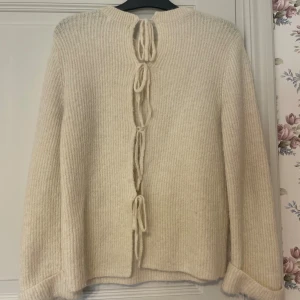 Beige stickad tröja med knyt från NA-KD - Superfin beige stickad tröja från NA-KD med unika knytband längs ryggen. Tröjan har rund halsringning, långa ärmar och ribbad struktur. Första bilden är alltså ryggen! Jättefin, bra skick! Sitter som en S.