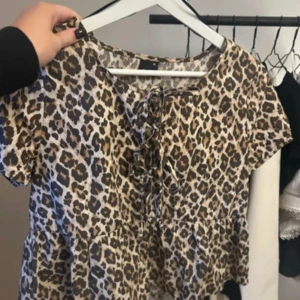 Leopardmönstrad blus med snörning - Säljer en kortärmad blus från Gina Tricot i leopardmönster. Toppen har snörning framtill och en lätt volang nedtill. Färgerna är beige, brun och svart. 