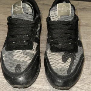 Valentino rockrunners - Snygga Valentino Garavani sneakers i svart och grått med camouflagemönster. Skorna har svarta snören, mesh- och mockadetaljer samt en platt sula. Perfekta för dig som vill ha en unik och trendig look med exklusiv känsla.