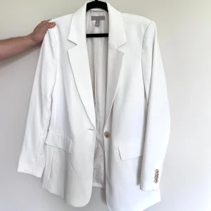 Vit kavaj - Snygg vit kavaj från H&M med klassisk krage, en knapp framtill och fyra dekorativa knappar vid ärmslutet. True to size. En liten fläck vid vänster ärmslut - se bild nr 3. Bara använd en gång - originalpris 499. Önskar du veta exakta mått? Tveka inte att höra av dig!