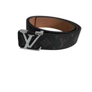 Louis Vuitton svart monogram bälte - Snyggt svart bälte från Louis Vuitton med klassiskt monogrammönster och stor LV-logga i silver på spännet. Bältet är gjort i exklusivt skinn och har en stilren, bred design som verkligen sticker ut. Perfekt accessoar för att lyfta din outfit.