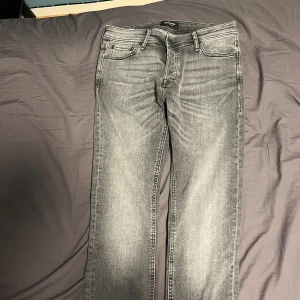Jack & Jones jeans - Slim Glenn jeans från Jack & Jones i snyggt grått med slitningar och klassisk femficksdesign. Modellen har slim passform och raka ben, med diskreta sömmar på bakfickorna. Perfekt för dig som gillar en modern och stilren look.