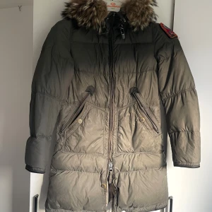 Parajumpers dunjacka med pälsluva - Snygg mörkgrön dunjacka från Parajumpers med stor pälsluva och ikonisk patch på ärmen. Jackan har dragkedja framtill, två snedställda fickor med knappar och quiltad design. OBS! Jackan är VÄL använd, har små defekter samt dragkedjor sönder på 3 ställen men som går att fixa med nya. Skriv för fler bilder. 