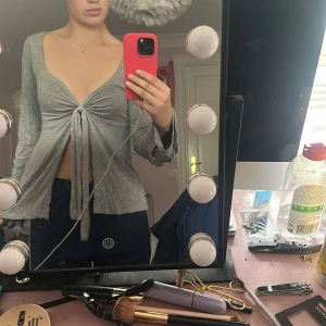 Grå långärmad omlottopp med knyt - Säljer en ljusgrå långärmad topp med djup v-ringning och knyt framtill. Toppen har vida ärmar och är tillverkad i mjukt bomullsmaterial. Snygg omlottkänsla och croppad framtill för en trendig look. Använt 3 gånger och den är lite för lång för mig i armarna ‼️☺️ super fin och jätte söt!! 