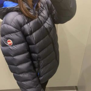 Mörkblå dunjacka Colmar med huva - Säljer en mörkblå dunjacka från Colmar med huva och dragkedja framtill. Jackan har ett quiltat mönster och en rund Colmar-logga på ärmen. Perfekt för kalla dagar och har en snygg, sportig look.