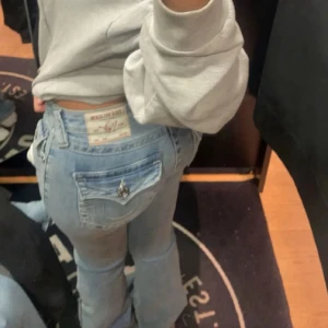 True Religon joey jeans  - Säljer ett par ljusblå jeans från True religon med bootcut passform och låg midja. Jeansen har snygga detaljer som fickor med lock och metallknapp bak, samt klassisk femficksdesign.Storlek 26 väldigt stretchiga. lite söndertrampade nertill men inget som man lägger märket till vid användning. 