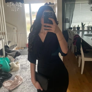 Svart omlottklänning från Zack - Säljer en svart omlottklänning från Zack med v-ringad hals och korta ärmar. Klänningen har en snygg drapering i midjan som ger en smickrande siluett. Perfekt för dig som gillar stilrena och eleganta plagg. Materialet känns mjukt och följsamt. Använt ungefär 3 gånger och säljer den då jag inte har någon användning av den längre 