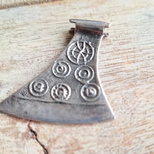 Vikingainspirerat yxformat halsband - Unikt halsbandshänge i form av en yxa, tillverkat i silverfärgad metall med cirkulära och spiralformade mönster. Hänget är ca 4 cm brett och har en cool, historisk vibe med detaljer som påminner om vikingatiden. Perfekt för dig som gillar mytologi och nordisk design.