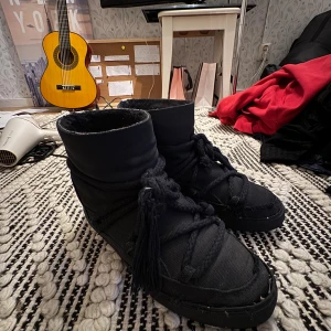 Svarta moon boots från Inuikii - Moon boots från Inuikii i svart textil med grova snören och dekorativa tofsar. Kan skicka mer bilder och ska tvätta dom helt 💗