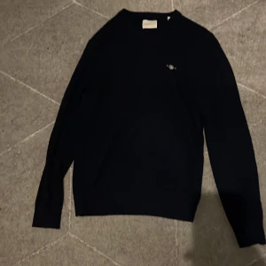 Svart GANT tröja i lammull, S - Svart tröja från GANT i extra fin lammull, med broderad logga på bröstet. Klassisk rund hals och långärmad modell, perfekt för dig som gillar stilrena och bekväma plagg. Passar dig som vill ha en enkel men snygg look.