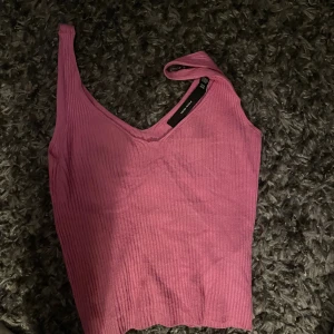 Rosa ribbad oneshoulder topp Vero Moda - Säljer en rosa ribbad topp från Vero Moda med oneshoulder-design. Toppen är ärmlös och har en snygg v-ringning. Perfekt för dig som gillar en trendig och unik look. Materialet är mjukt och stretchigt för en bekväm passform.