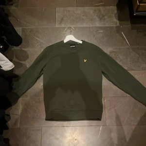 Grön sweatshirt från Lyle & Scott - Säljer en snygg grön sweatshirt från Lyle & Scott. Den har en klassisk design med rund hals och ett litet gult emblem på bröstet. Perfekt för både vardag och chill. Tröjan är i bra skick och passar perfekt till höst- och vårgarderoben. 🐥