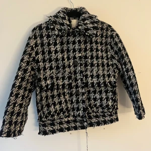 Svartvit rutig jacka - Säljer en svartvit jacka med grovt rutigt mönster och fransiga kanter. Jackan har stor krage, knappar framtill och långärmade ärmar. Materialet är stickat och ger en cool, chunky vibe. Perfekt för dig som gillar statement-plagg och vill sticka ut.