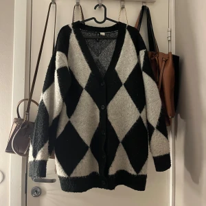 Svartvit rutig kofta från H&M - Säljer en oversized kofta från H&M i storlek S med svartvita rutor i ett snyggt harlequinmönster. Koftan har v-ringning, knappar framtill och är stickad i mjukt material. Perfekt för dig som gillar statement-plagg och vill ha en chill vibe.