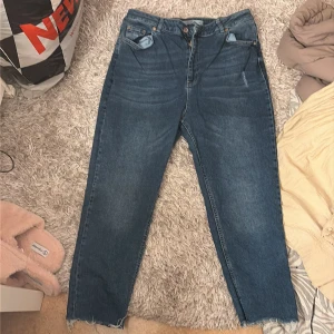 Blå jeans från LCW Jeans, storlek 46 - Säljer ett par klassiska blå jeans från LCW Jeans i storlek 46. Modellen har raka ben med rå kant nertill, fem fickor och knappstängning. Jeansen har en normal passform och är tillverkade i slitstarkt denimtyg. Perfekt för dig som gillar enkel och tidlös stil.