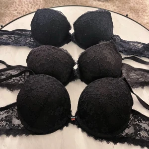 Tre stycken bh ar 2st svarta och 1st mörkblå - Säljer tre stycken bh-ar med snygga spetsdetaljer och vadderade kupor. Toppen har axelband och genomgående spets längs sidorna och kuporna, vilket ger en elegant och feminin look. Perfekt för dig som gillar stilrena och klassiska plagg med lite extra edge. Den svarta med körsbär i mitten är ifrån new yorker 