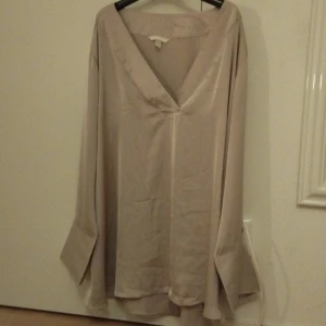 Beige sidenblus med v-ringning H&M - Säljer en lyxig beige blus från H&M i storlek XXL. Blusen har en djup v-ringning, långa vida ärmar och är tillverkad i glansigt sidenmaterial som ger en elegant känsla. Perfekt för dig som gillar oversized och flowy stil.