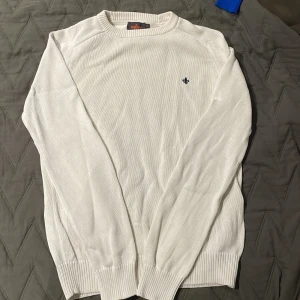 Vit stickad tröja från Morris XS - Snygg vit stickad tröja från Morris i storlek XS. Tröjan har rund hals, ribbade muddar och ett diskret Morris-emblem broderat på bröstet. Perfekt för dig som gillar klassisk och clean stil med en touch av preppy. Ny pris ca 1300