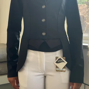 Tävlings minifrack  - Snygg svart ridkavaj från Horse In med klassisk design och fyra silverfärgade knappar framtill. Kavajen har figurnära passform, lång ärm och är tillverkad i stretchigt lycra-material för extra komfort. Perfekt för dig som vill ha stil på tävling eller träning nypris 2500.
