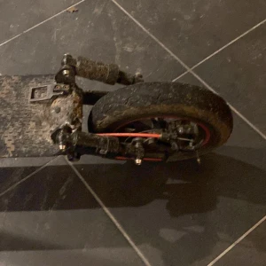 Elektrisk sparkcykel - Elektrisk sparkcykel med svarta och röda detaljer. Stora hjul för stabil körning. Synligt smutsig och sliten, särskilt på däcken och fotplattan. Passar för pendling eller fritid. Fungerande bromssystem och stöd. Säljs i befintligt skick.