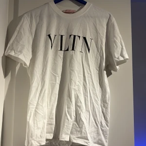 Vit VLTN t-shirt från Valentino - Snygg vit t-shirt från Valentino med VLTN-tryck i svart på bröstet. Klassisk rund hals och korta ärmar. Tillverkad i mjuk bomull, perfekt för en clean och stilren look. Made in Italy.