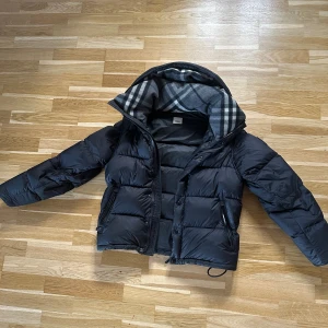 Svart pufferjacka med huva - Burberry vinter jacka/väst, storlek M, skick 9/10. Köpt från känd reseller från Facebook market. Bevis finns. Äktehets garanterat. Har sålt flera saker på Facebook grupper. Bevis finns där med.