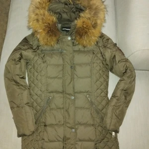 Olivgrön dunjacka Rockandblue - Säljer en olivgrön dunjacka från Rockandblue med äkta päls på huvan och quiltade detaljer. Jackan har dragkedjor på fickorna, tryckknappar framtill och en patch på ärmen. Perfekt för kalla dagar med sin varma och stilrena look. Använd fåtalet ggr så i mycket fint skick! 