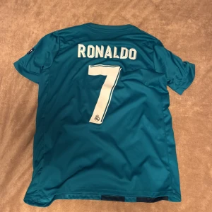 Real Madrid Ronaldo tröja Adidas S - Säljer en officiell Real Madrid fotbollströja med Ronaldo och nummer 7 på ryggen. Tröjan är blå med mörkblå pixelmönster, vita tryck och FIFA World Champions 2017-märke. Adidas logga och Fly Emirates sponsor på bröstet. Materialet är lätt och andas, Climacool.
