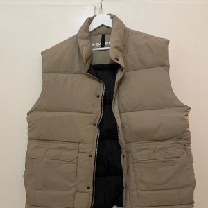 Vintage Everest Väst - Beige vintage dunväst från Everest med PlatinaFlexSystem. Västen har hög krage, två stora fickor framtill och dragkedja.