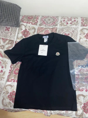 Svart Moncler t-shirt i bomull - Svart t-shirt från Moncler i mjuk bomull med klassisk rund hals och korta ärmar. På bröstet sitter Monclers ikoniska logotyp. Enkel och clean design som passar perfekt till jeans eller shorts.