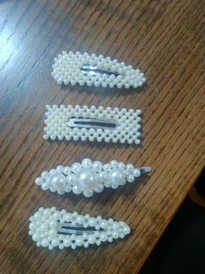 Fyra hårspännen med pärlor - Säljer fyra snygga hårspännen dekorerade med vita pärlor i olika former och mönster. Perfekta för att ge frisyren en extra touch av elegans och trendig stil. Passar både till utsläppt hår och uppsättningar.