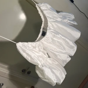 Romantisk puffig blus - Vit glättad off shoulder-blus från Reclaimed Vintage, som ny! Använd EN gång. Köpt online på Asos.com, i storlek 34. Mått: längd 35 cm, midjevidd 66 cm (kan töjas ut till 100 cm). Material: 100% polyester.