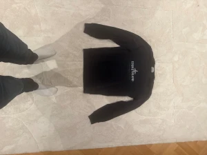 Svart långärmad tröja Stone Island - Svart långärmad tröja från Stone Island med vit logotyp och text på bröstet samt en mindre logga på ärmen. Tröjan är i mjuk bomull och har en klassisk, normal passform. Perfekt för dig som gillar stilrena och ikoniska streetwear-plagg.