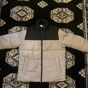 Beige och svart pufferjacka Jack & Jones - Säljer en beige och svart pufferjacka från Jack & Jones i storlek M. Jackan har hög krage, dragkedja framtill och två sidofickor. Fodret är svart och jackan är perfekt för kyliga dagar. Enkel, stilren design som funkar till det mesta.