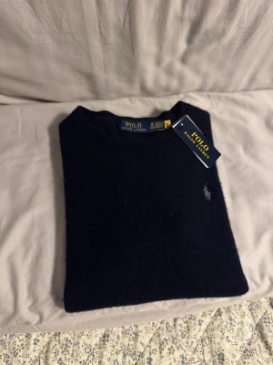  Polo Ralph Lauren stickat tröja - Snygg marinblå tröja från Polo Ralph Lauren i mjuk kashmir. Klassisk rund hals och diskret broderad logga på bröstet. Perfekt för dig som gillar stilrena och lyxiga plagg med skön känsla. Taggarna sitter kvar.