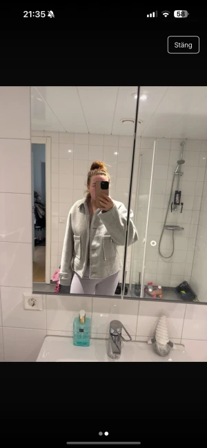 Jacka - Säljer en stilren grå overshirt med stora fickor framtill och knappar längs hela framsidan. Jackan har en klassisk krage och långa ärmar med knappdetalj vid mudden. Perfekt för lager-på-lager och chill stil.