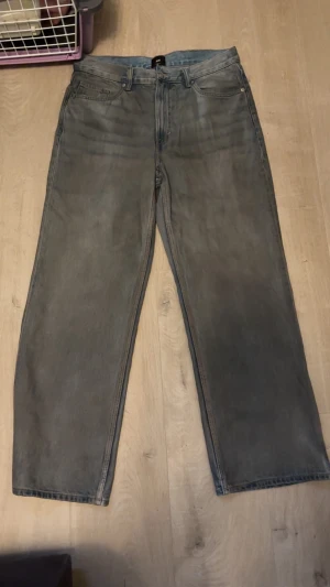 Grå raka jeans från H&M - Säljer ett par grå jeans från H&M med klassisk femficksdesign och raka ben. Jeansen har normal passform och är tillverkade i ett mjukt bomullstyg med en lätt tvättad look. Perfekta för en chill och stilren vardagsoutfit.