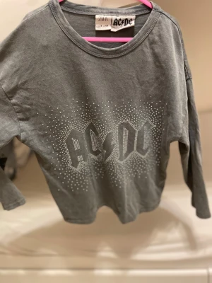 Grå AC/DC långärmad tröja från Zara - Cool grå långärmad tröja från Zara med AC/DC-tryck framtill i silvriga prickar. Rund hals och mjukt bomullsmaterial som är skönt mot huden. Perfekt för dig som gillar bandtröjor och vill ha en avslappnad stil. Barn till tjejer 