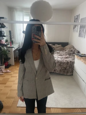 Rutmönstrad kavaj - Stilren rutmönstrad kavaj i beige/grå. Lätt oversized passform med enkel knäppning och fickor framtill. Bekväm, modern och i mycket fint skick. Perfekt till både vardag och jobb.