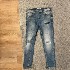 Ljusblå jeans med slitningar - Snygga blå skinny jeans med slitningar och hål på benen för en cool, avslappnad vibe. Klassisk femficksmodell med knapp och dragkedja fram. Jeansen har en ljus tvätt och smal passform som sitter tajt längs benen.