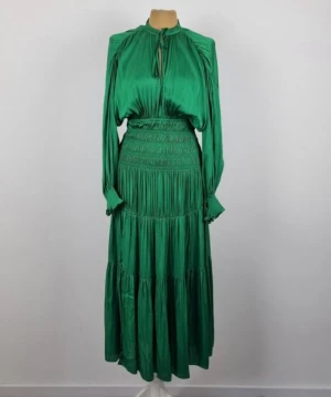 Grön långklänning från Maje - Snygg smaragdgrön långklänning från Maje glansigt material. Klänningen har långa puffärmar, smockad midja och volangdetaljer. Rund halsringning med knytband och lätt rynkade partier ger en lyxig och flowy känsla.