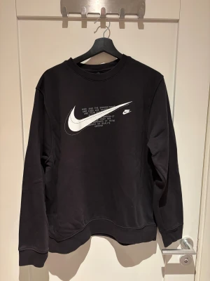 Svart Nike sweatshirt med vit logga - Svart sweatshirt från Nike i storlek M med stor vit Swoosh-logga och text på bröstet. Tröjan har används ett fåtal gånger, men är annars i ny skick. 
