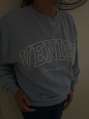 Ljusblå sweatshirt med Venice-tryck - Snygg ljusblå sweatshirt med stort vitt tryck 'VENICE' och texten 'Los Angeles, CA' framtill. Tröjan har rund hals, ribbade muddar och en loose passform. Från HM tidigare sortiment, finns ej att köpa längre. Storlek S