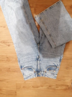 Ljusblå raka jeans i storlek 34 - Ljusblå jeans med raka ben och klassisk femficksdesign. Jeansen har hög midja och råa kanter nertill för en avslappnad vibe. Tillverkade i denim med snygga kontrastsömmar. Perfekta för dig som gillar en tidlös och chill look. De är använda, men har lite slitningar. Annars inga defekter eller repor. 